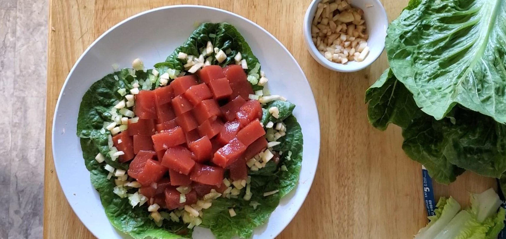 A white plate, with cubes of red gelatin on a bed of lettuce, surrounded with chopped celery.