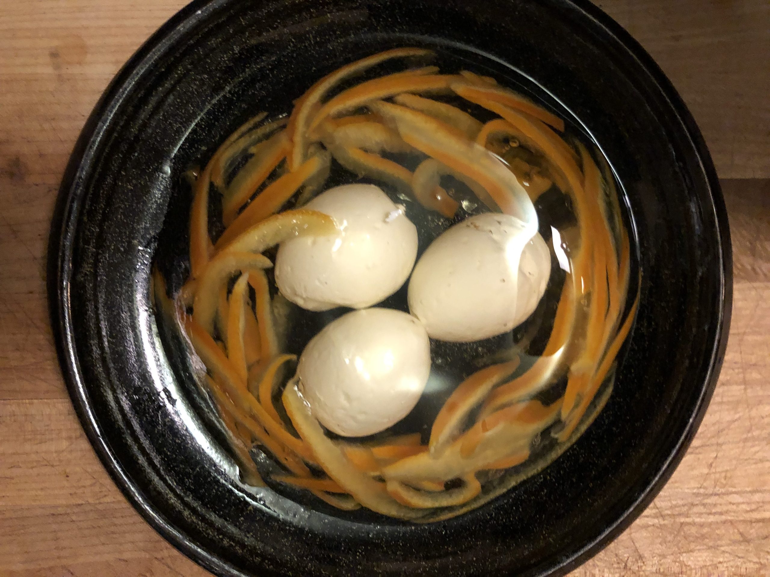 Three white eggs within a clear dome surrounded by candied orange peels to look like a nest.