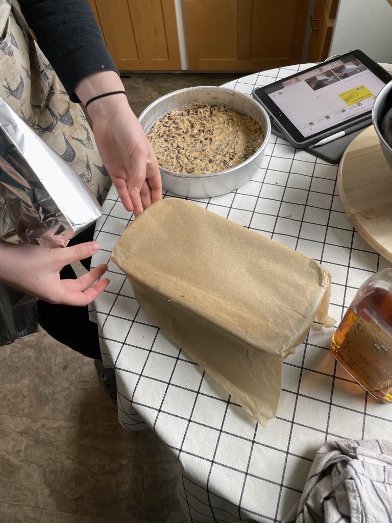 A woman covers a loaf pan with parchment paper, another uncovered cake pan is on the table.