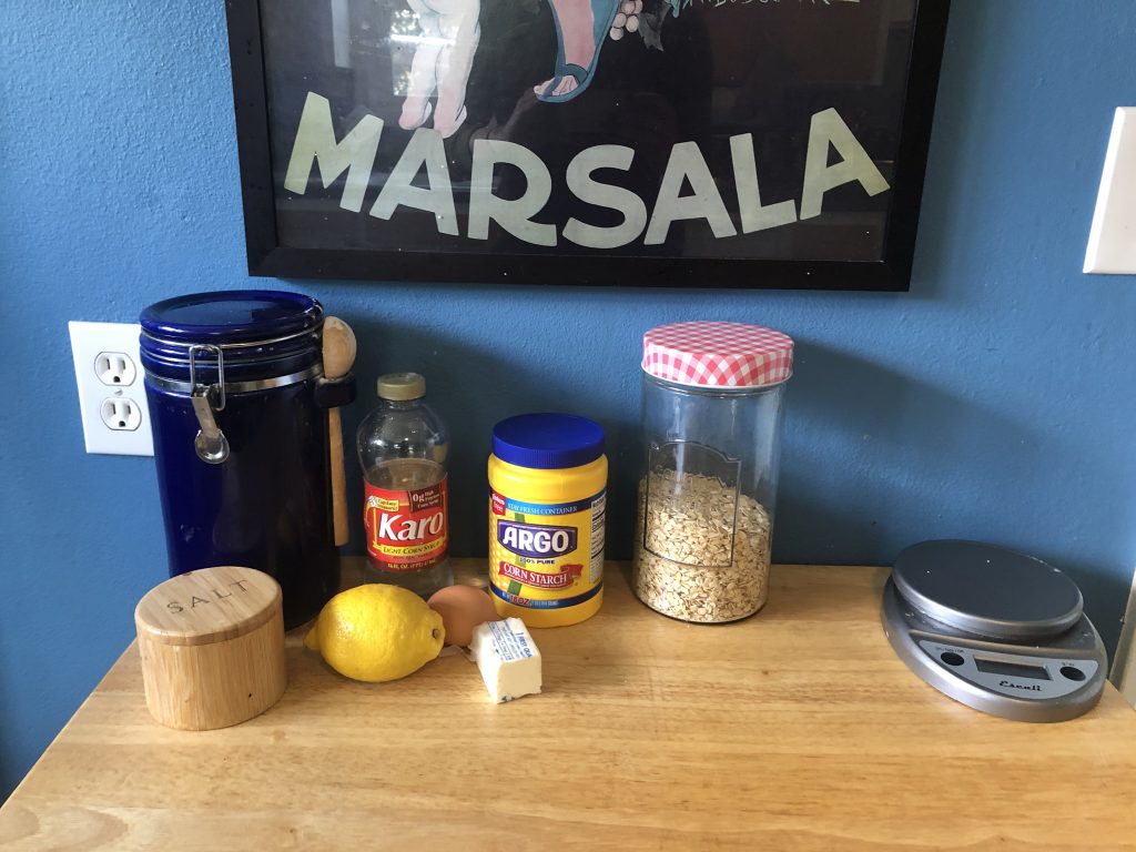 Sugar, corn syrup, cornstarch, oats, salt, lemon, an egg and butter sit on a counter.