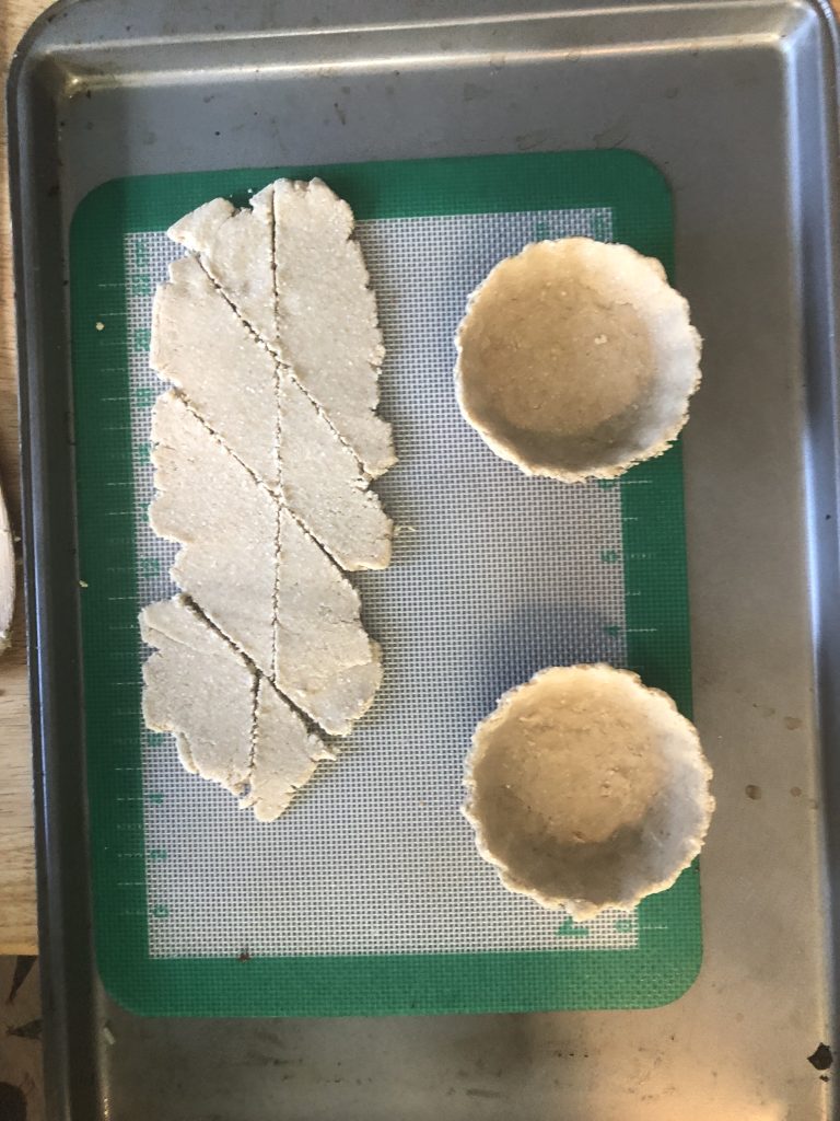 Two tiny baked tart shells, next to light white baked crust cut into diamonds.