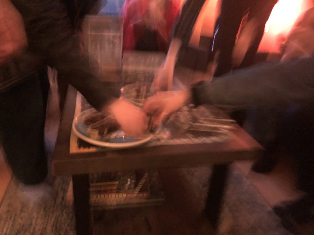 Three blurry hands reach for slices of fruit cake on a large coffee table.