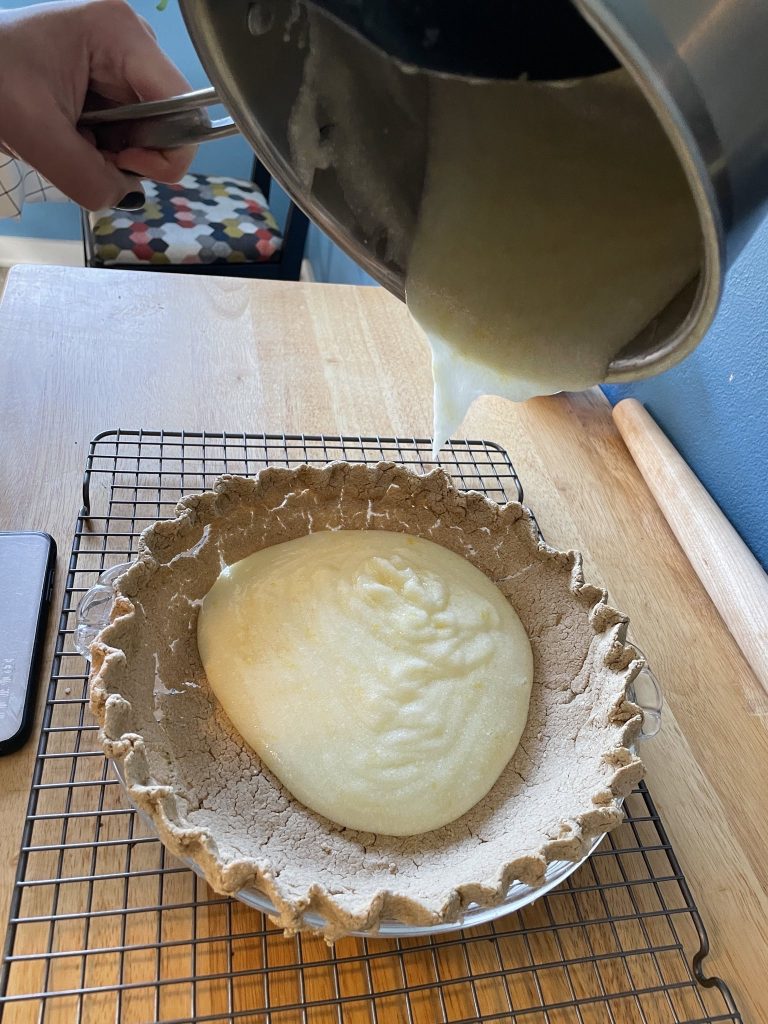 pouring a small amount of lemon filling into a cracked oat crust pie shell.