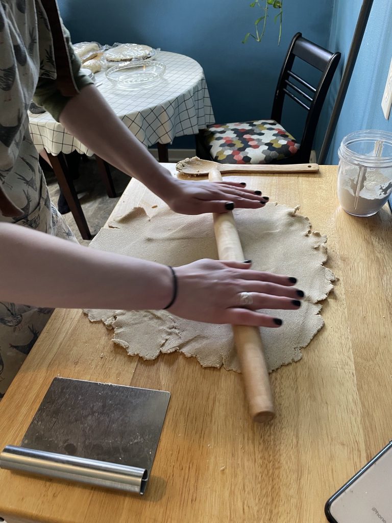 a woman uses a rolling pin to roll dough into a rough circle.
