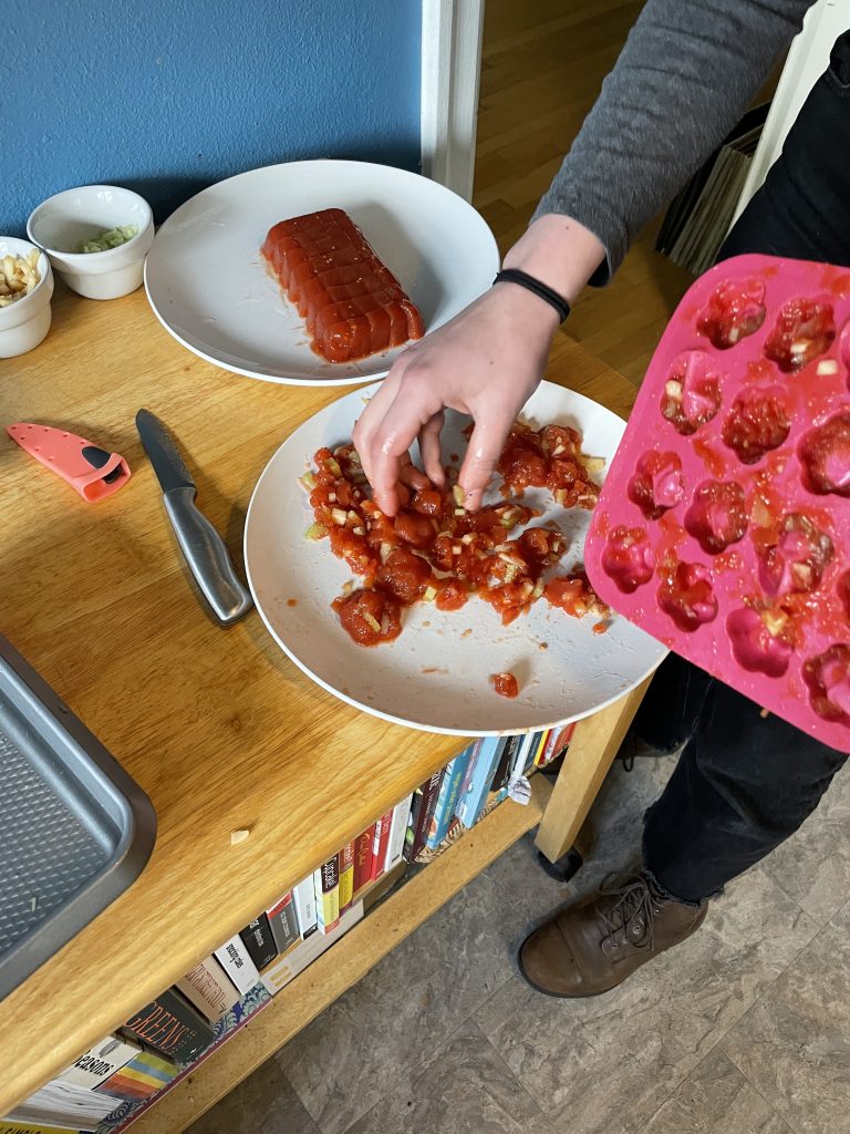 Red tomato aspic in a pink icecube tray, some of it is on a plate and looks like raw meat.