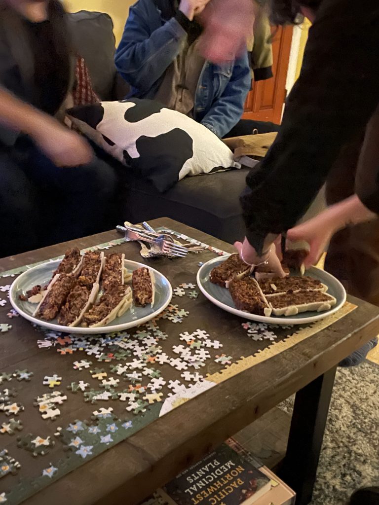 slices of fruit cake on plates on a coffee table surrounded with people.