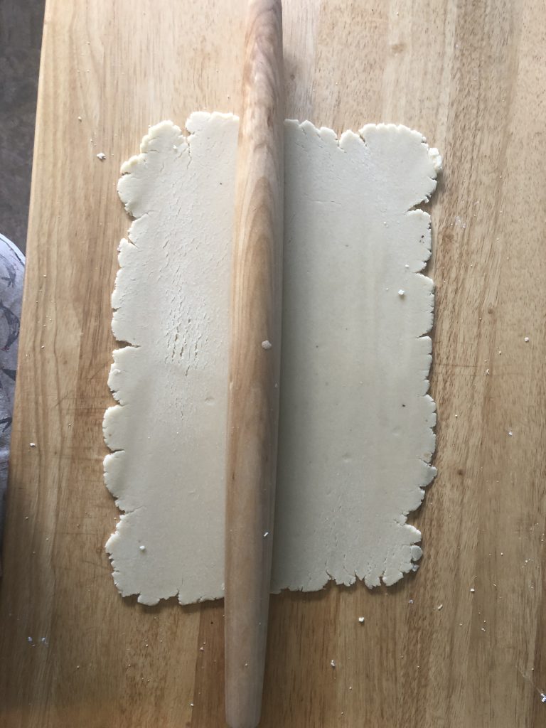 A rolled out square of almond paste with a rolling pin.