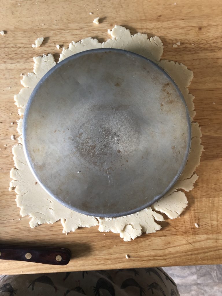 a rough circle of almond paste with a circular cake pan on top of it.