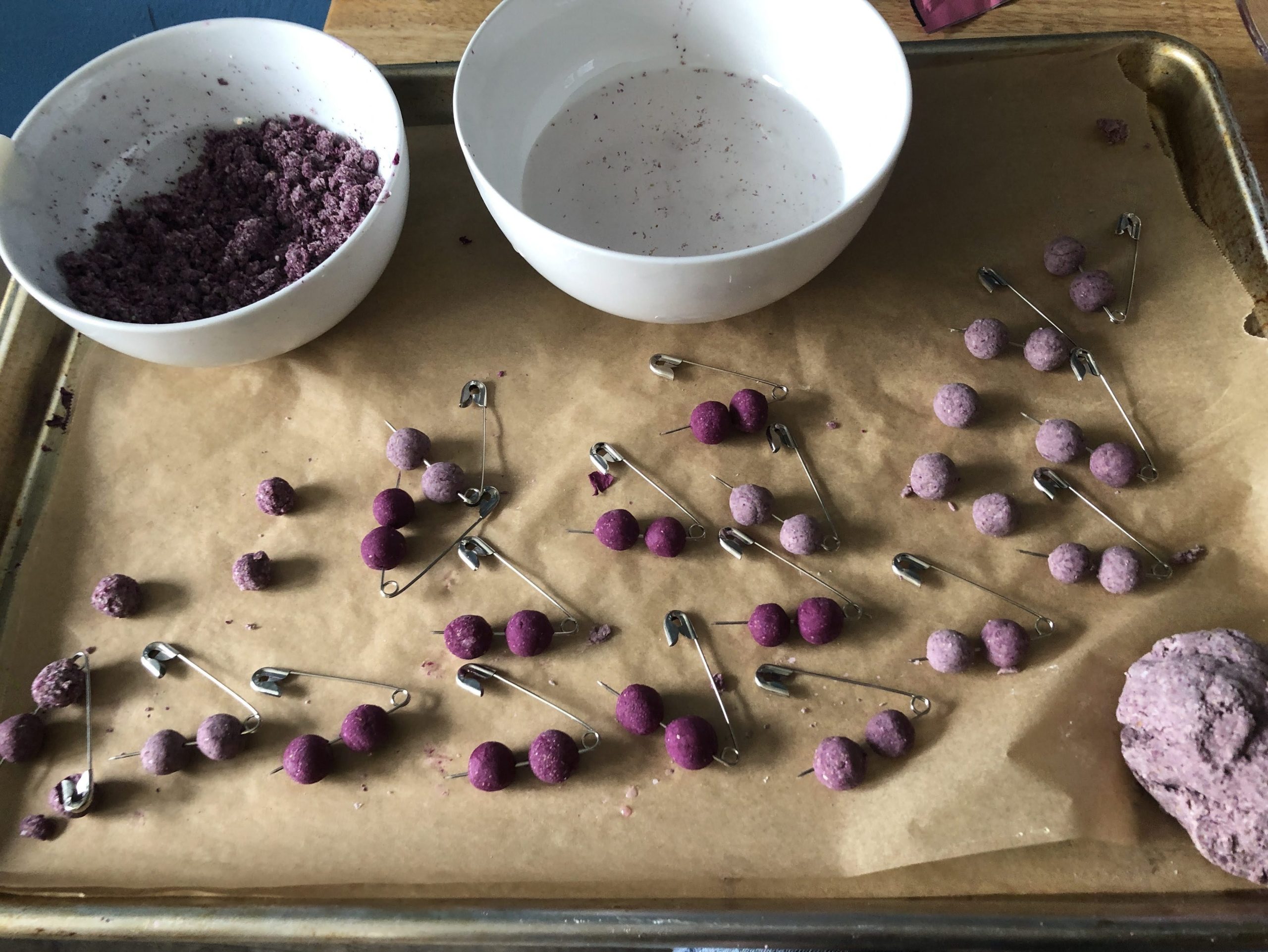 round balls of purple and grey clay impaled on safety pins.