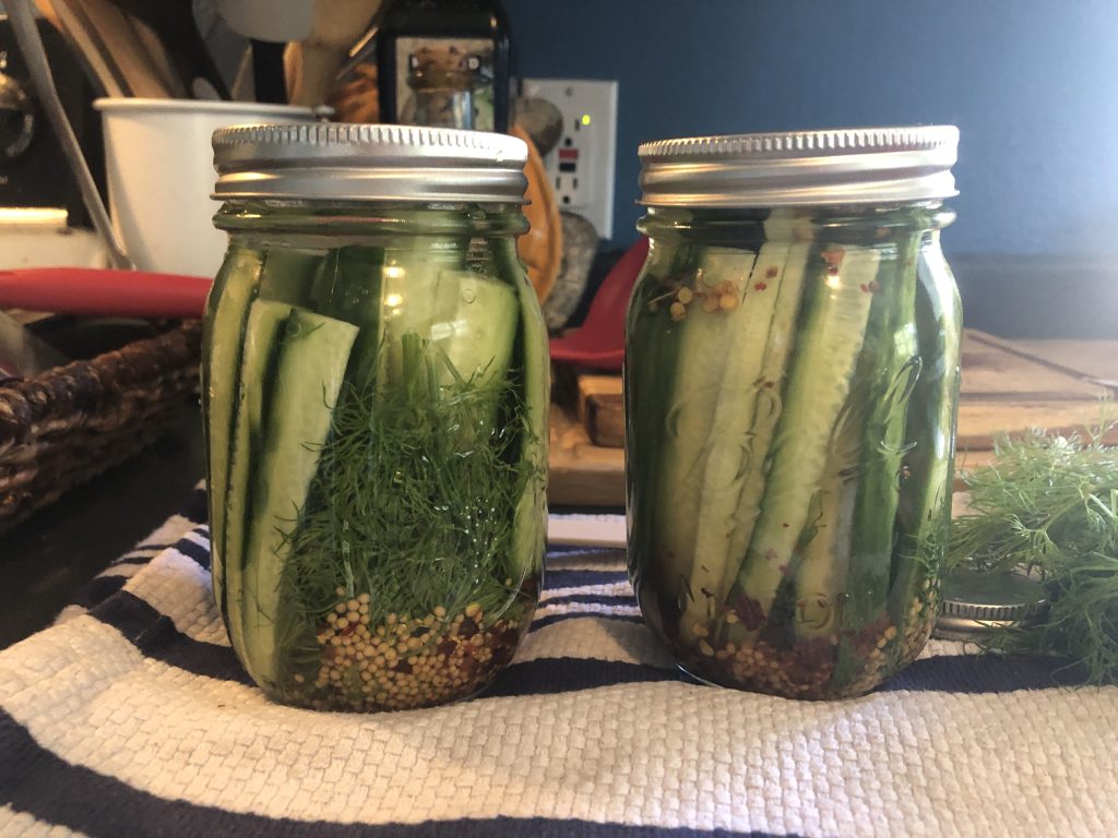 Two jars of speared pickles with dill and mustard seeds, the cucumbers are a fresh bright green.